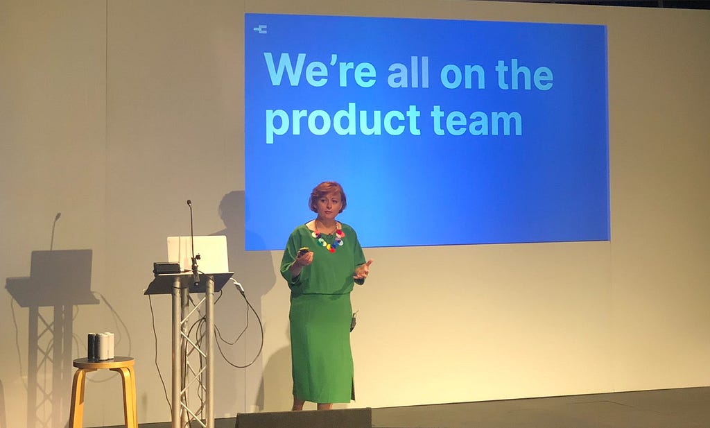 Rachel Coldicutt speaking on stage at the Camp Digital conference with “We’re all on the Product team” written in large font on a slide behind her. Photograph by Emma Parnell