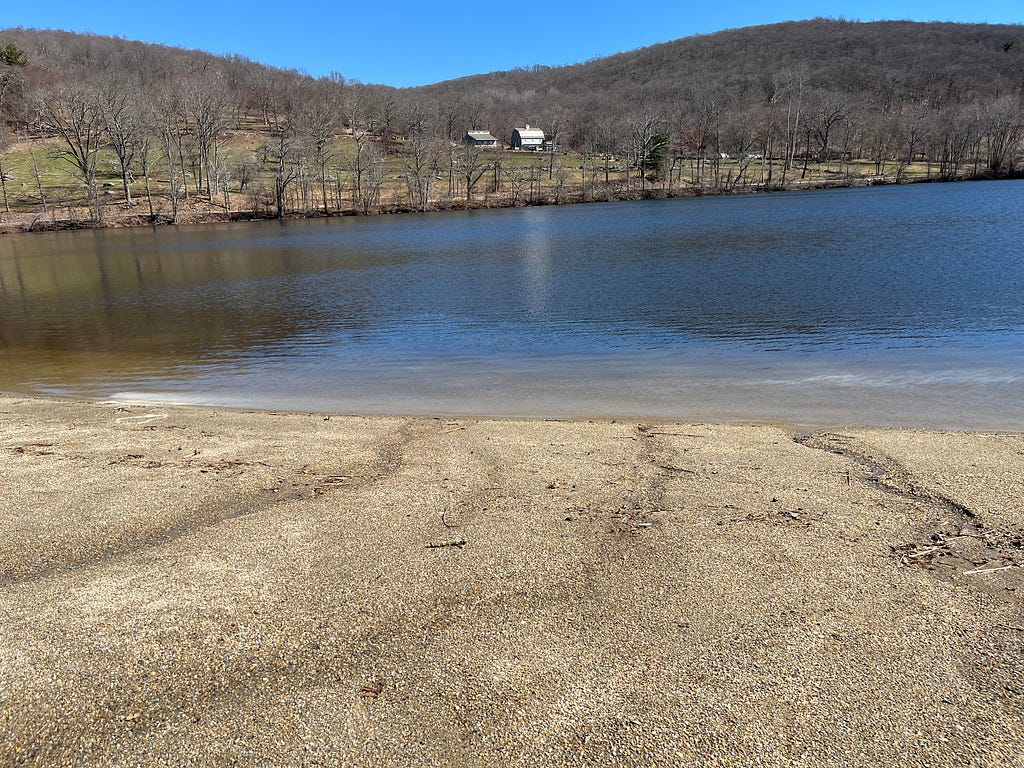 Photo of sandy beach area at a lake with my son’s white ashes floating and settling into the water