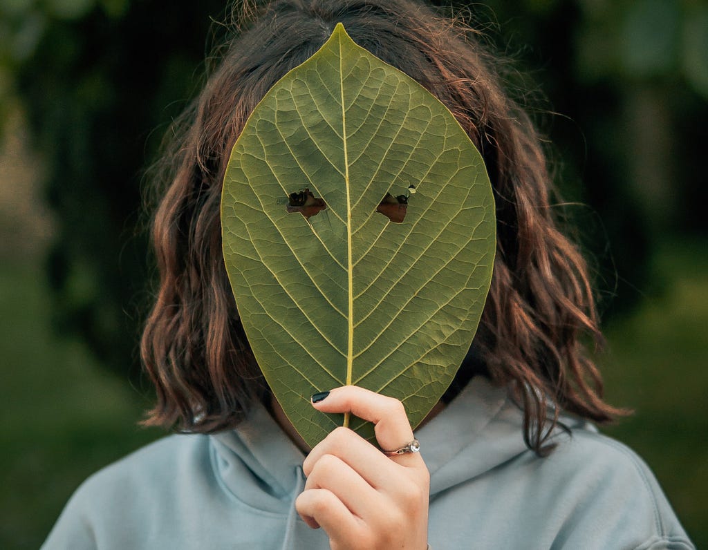 Woman hiding her face behind a leaf with two eyeholes