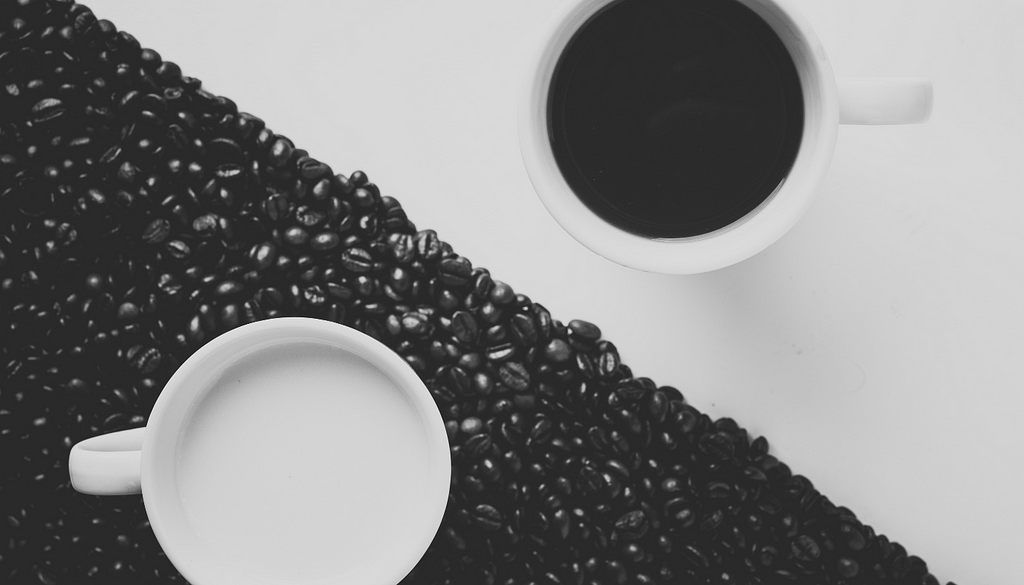 Image of table with coffee beans laid out on half, split diagonally. A mug on each side of the diagonal.