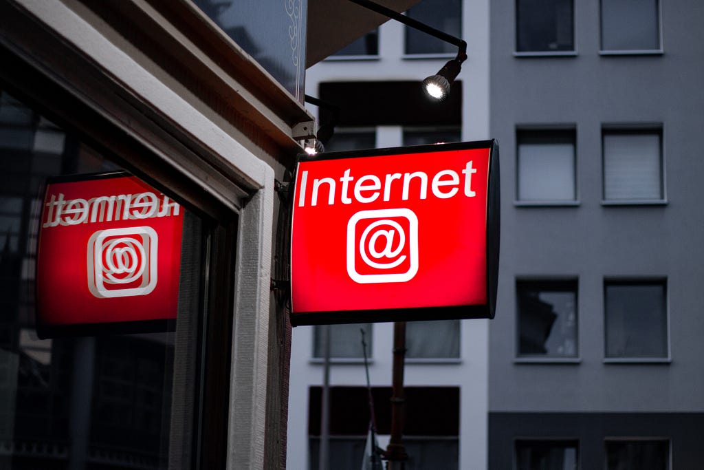 A red sign reading “Internet” in white text, with an at symbol in white beneath it, hanging on the side of a building.