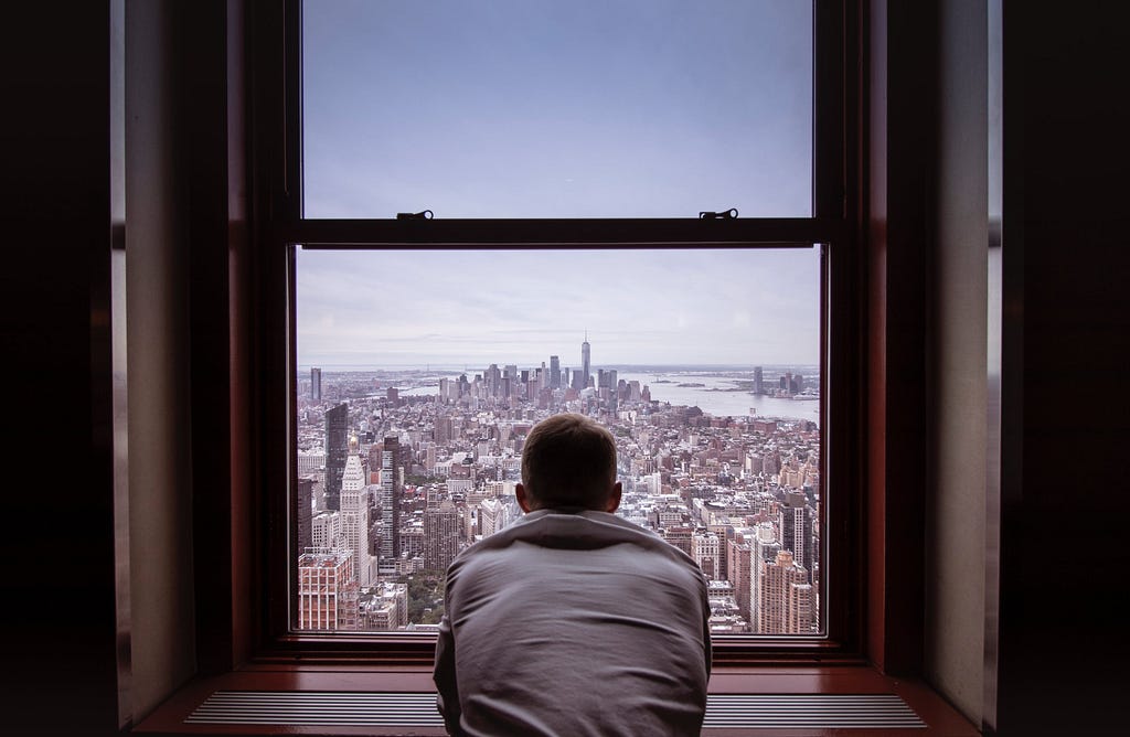 A man, staring out at the NYC skyline, in melancholy