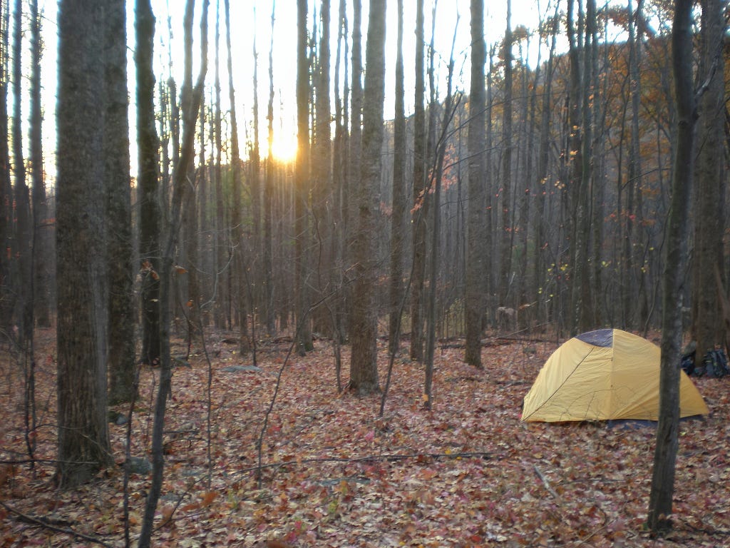 A photo with a forest, a tent and a rising sun. Small improvements have been made.