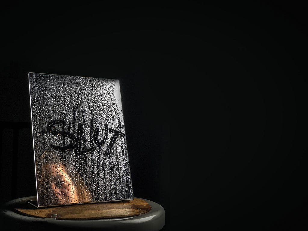 A woman in a dark room looking into a small wet mirror with the word “slut” drawn through the wet surface.