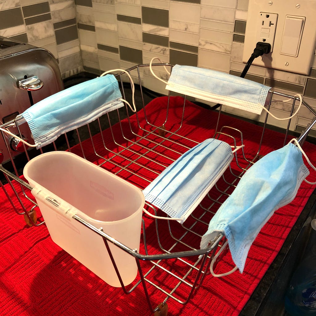 Photo of a metal drying rack with a red towel underneath. Four surgical masks are drying on it.