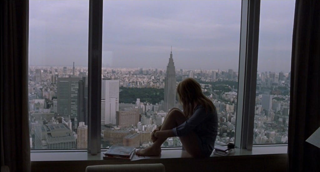Cena do filme estadunidense Lost In Translation (Encontros e Desencontros) de Sofia Coppola. Na cena aparece a protagonista Charlotte sentada encolhida com as mãos á frente do joelho, na beira da janela no alto de um prédio olhando para a fora.