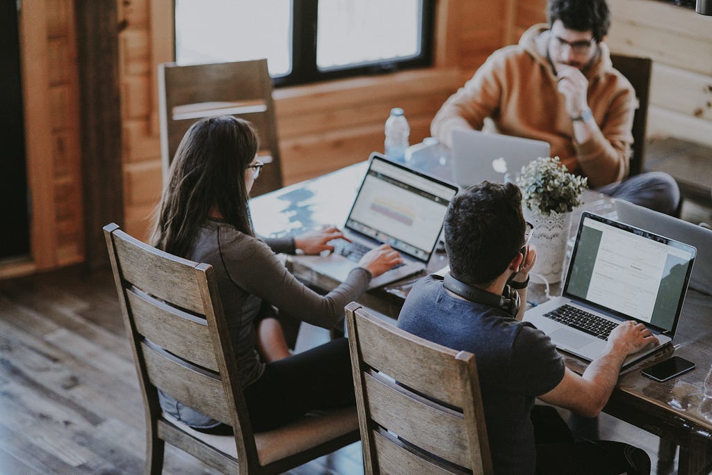 Two men and a woman are sitting together, each working on a different laptop.