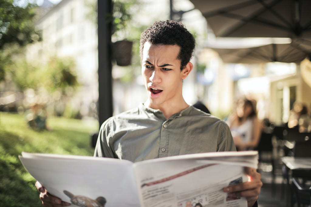 A man with a shocked expression reading a newspaper.