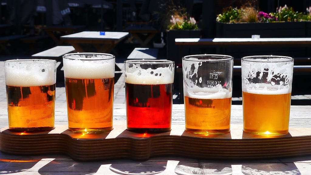 Cinco copos de cerveja puro malte lado a lado em cima de uma base de madeira.
