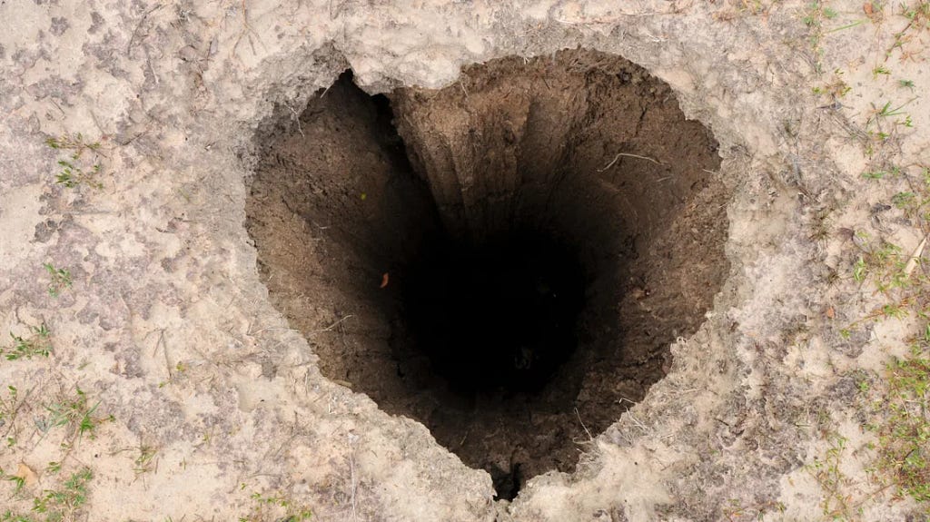 Deep hole in the ground with a vague heart shape to its entrance.