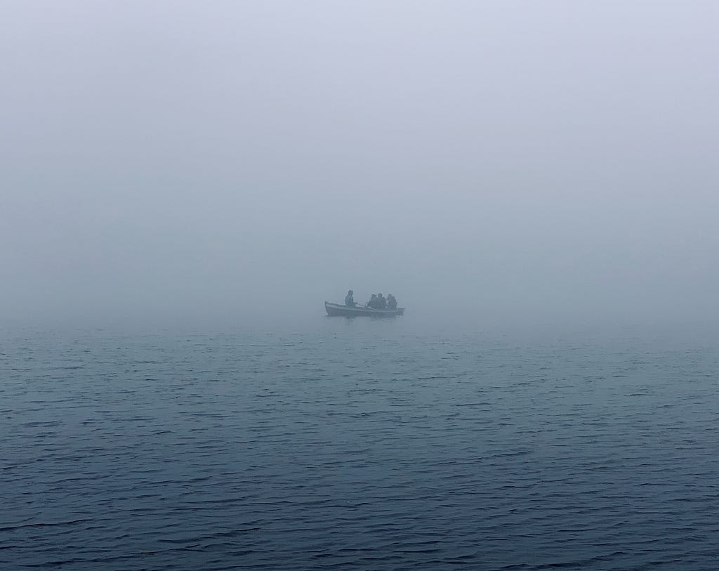 In the distance, a boat floats alone in a body of water, bathed in fog.