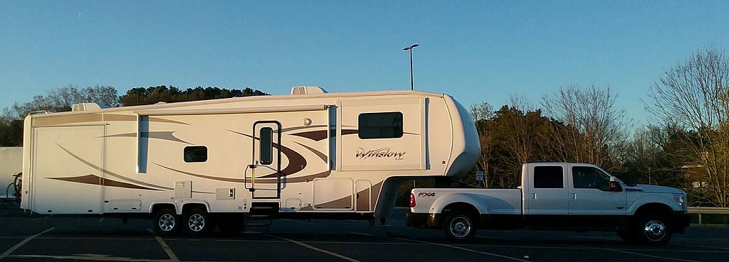 A wide angle shot of a long recreational vehicle hitched to a white pickup truck.