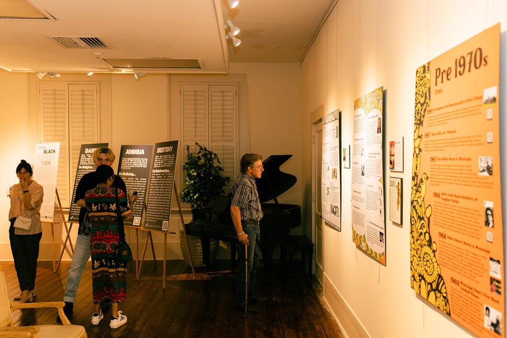 This image shows people talking and viewing the timeline panels of MS LGBTQ+ history at the magnolia memories exhibit.