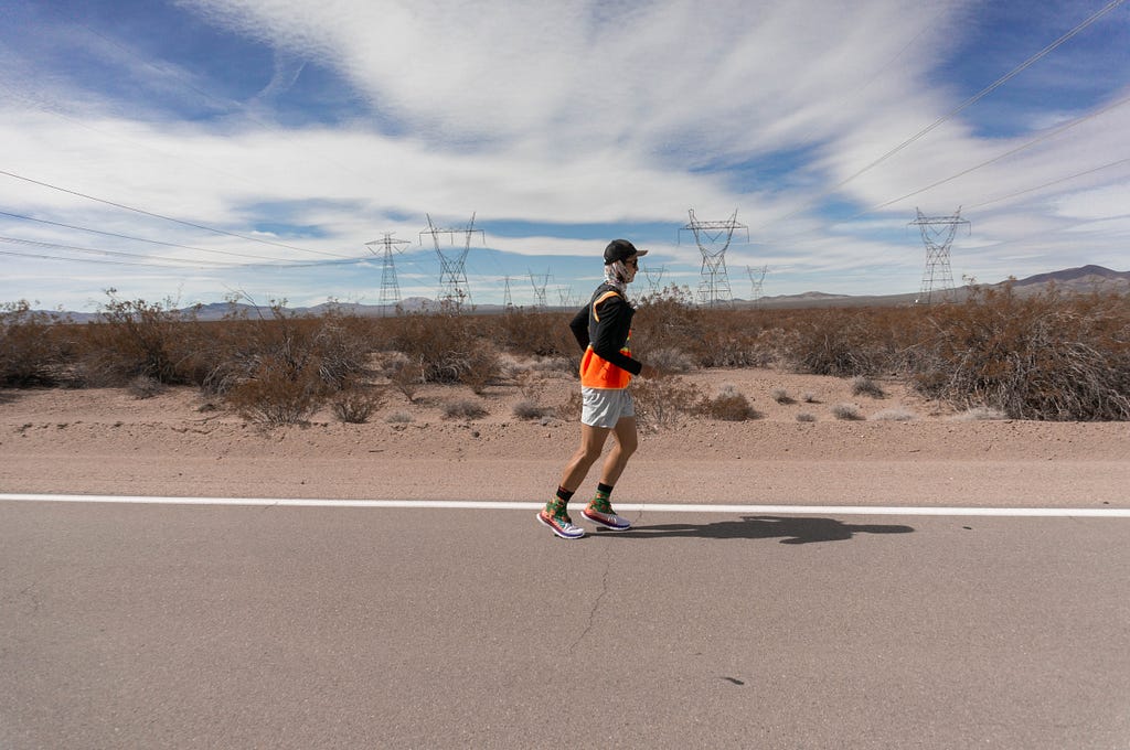 Runner on the side of a road in the foreground with desert brushes in the background along with long distance powerlines