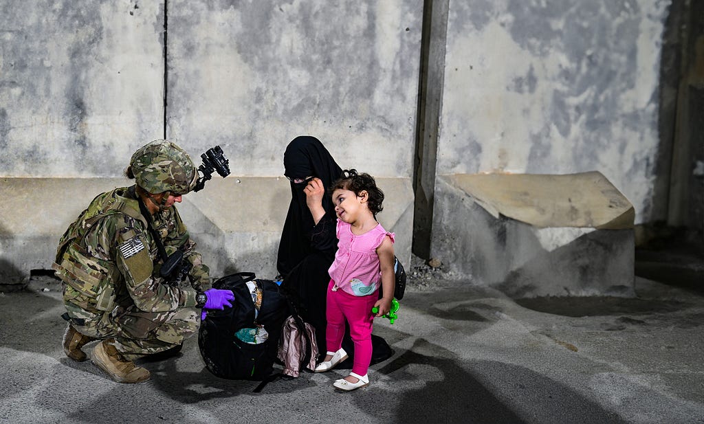 A U.S. paratrooper helps a woman and child evacuating from Afghanistan in August 2021. Photo by U.S. Central Command Public Affairs