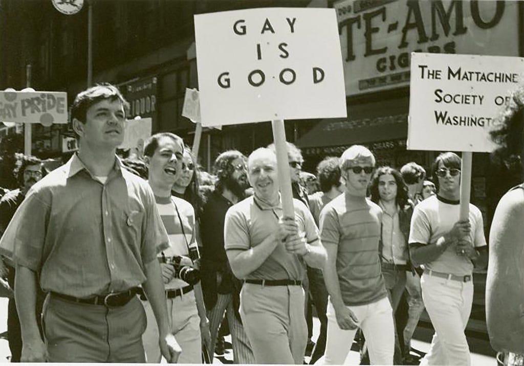 Frank E Kameny holds a sign saying “Gay is Good”. The picture is in black and white.