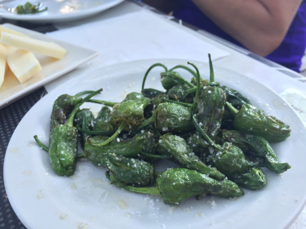 A white plate with a heap of green, cooked peppers
