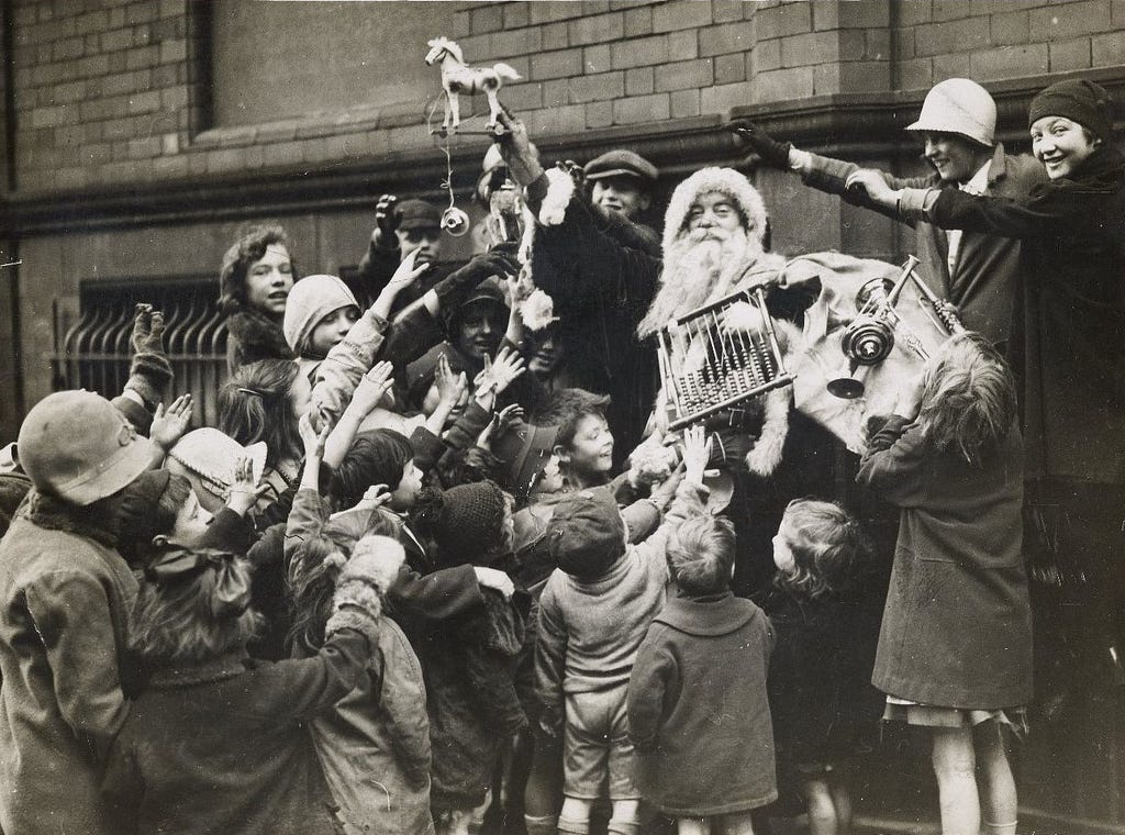 Black and white photograph of Father Christmas handing out presents to a crowd of children from the Wood Street Mission in Manchester in the 1930s