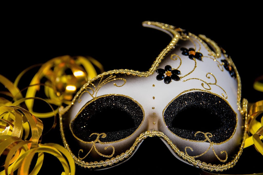 Venetian stlyle carnival mask. It is shown on a black background, the mask is white, with flower ornaments and gold laces