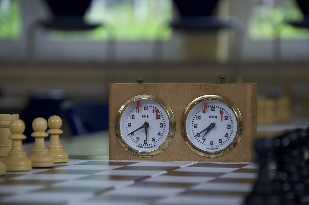 White pieces on left, black ones on right. Analog clock in middle with red flags. Left button pressed, so black to move.