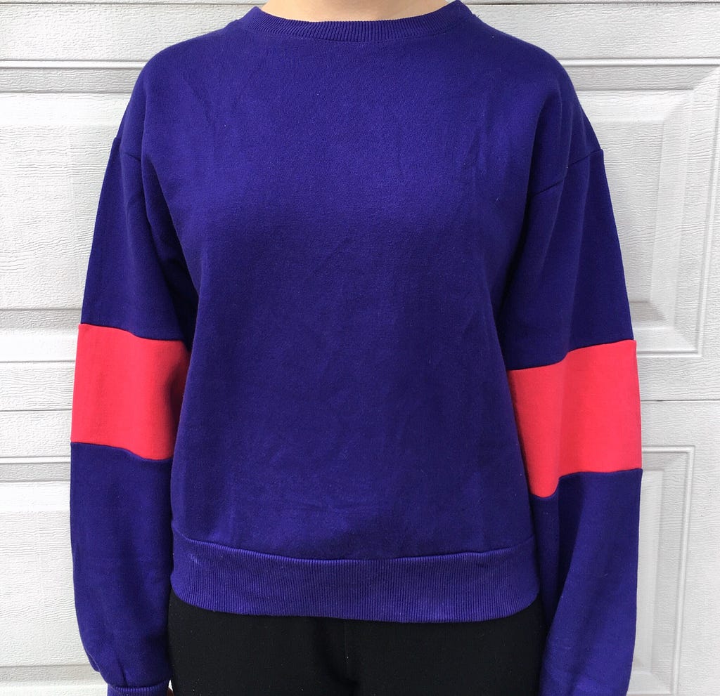 A large purple sweater with pink color blocked sleeves. Worn with black joggers.