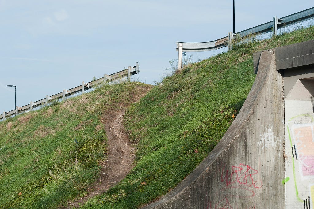 A broken barrier on a roadway and a worn path leading down the side of a hillside. It’s almost as though someone had broken through the barrier to provide a shortcut that many others have taken. The image suggests that a shortcut may create more problems than it solves.