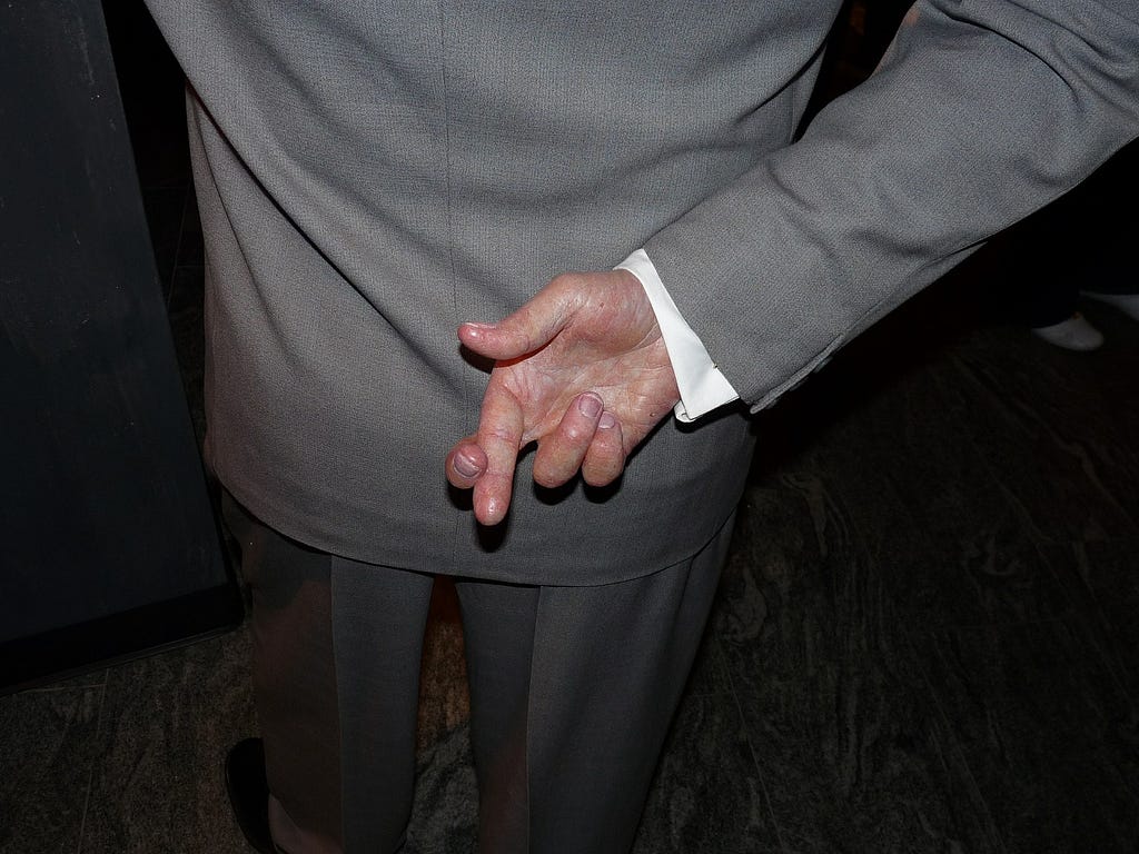 Photograph of the back of a white man who is crossing his fingers (behind his back)