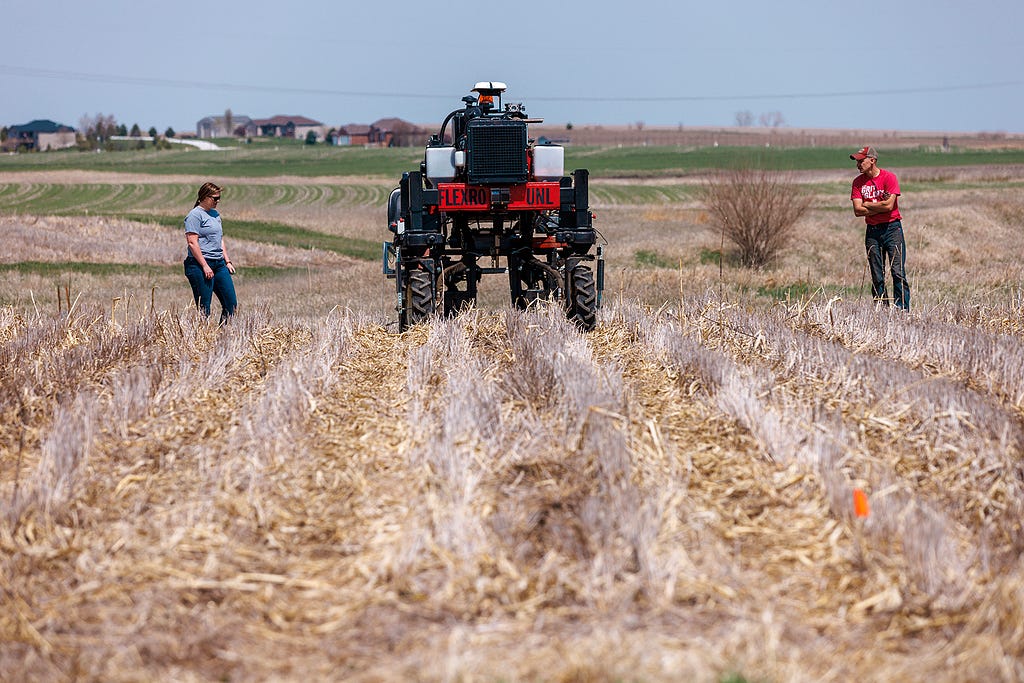 Graduate research assistant Taylor Cross (left) and graduate student Ian Tempelmeyer walk behind the Flex-Ro autonomous planting robot as it starts a row at Rogers Memorial Farm, east of Lincoln.