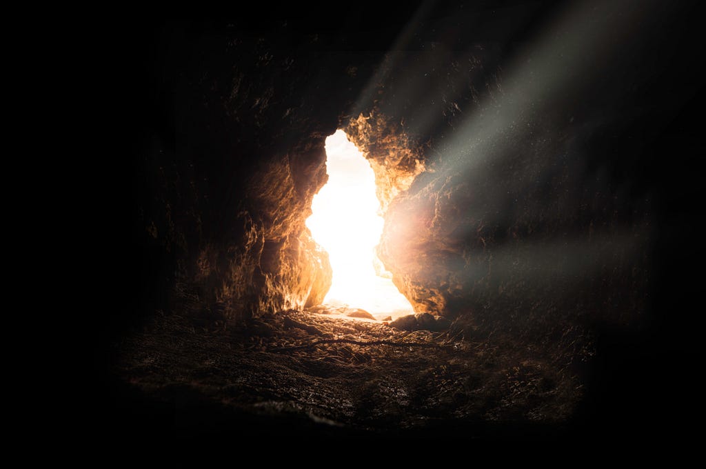 photo of a cave opening, with shining light coming in