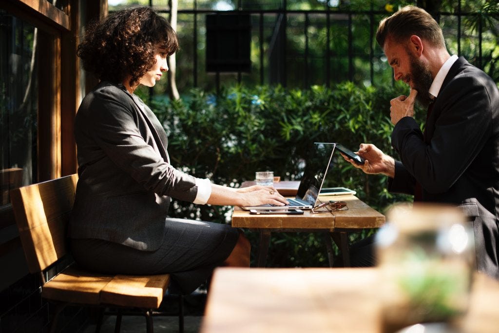 Two Freelancers/Consultants working on devices at a sunny outdoor café.