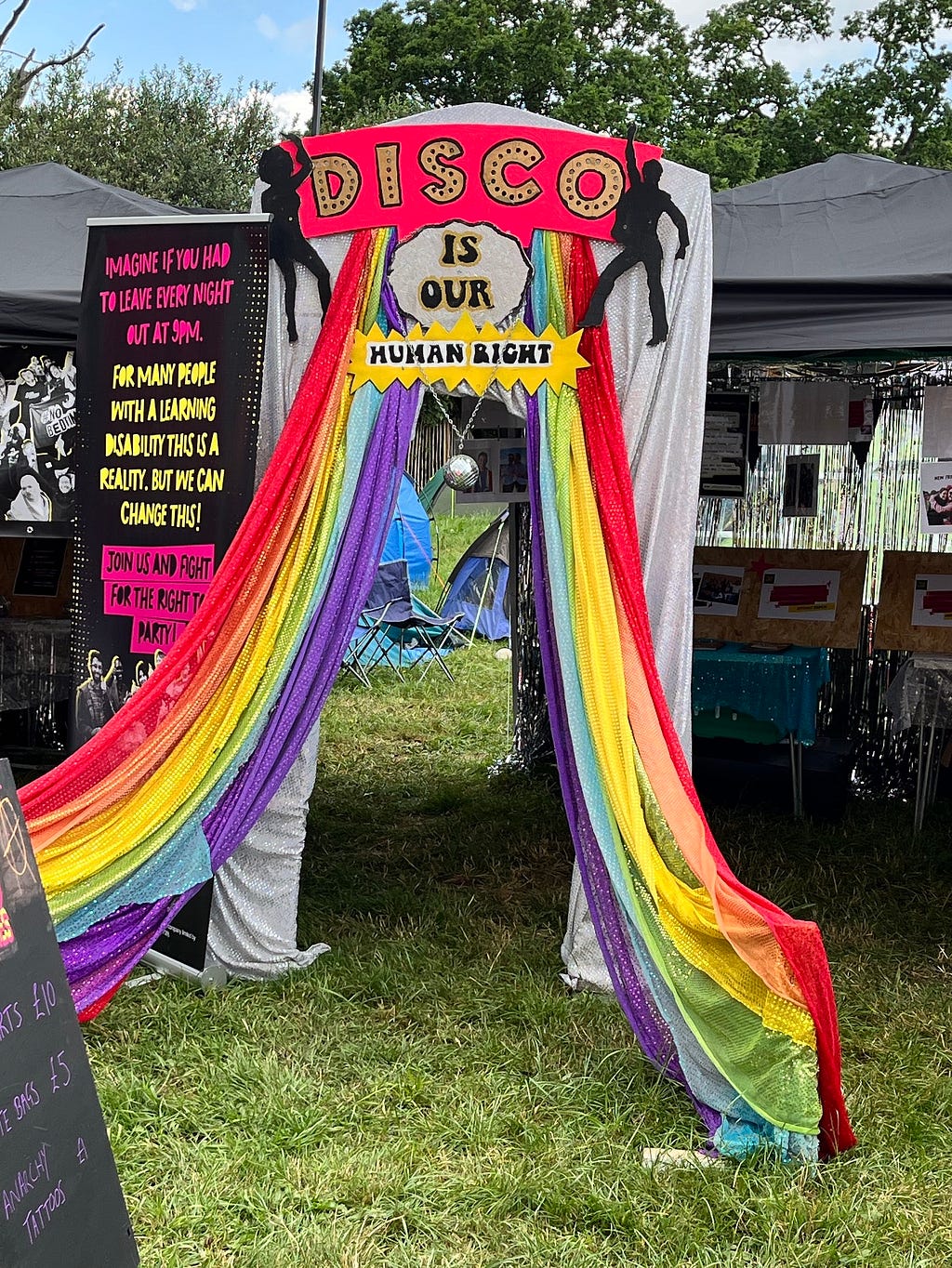 Archway to a tent draped in sparkly rainbow colours and saying ‘Disco is our human right’ above the entrance.