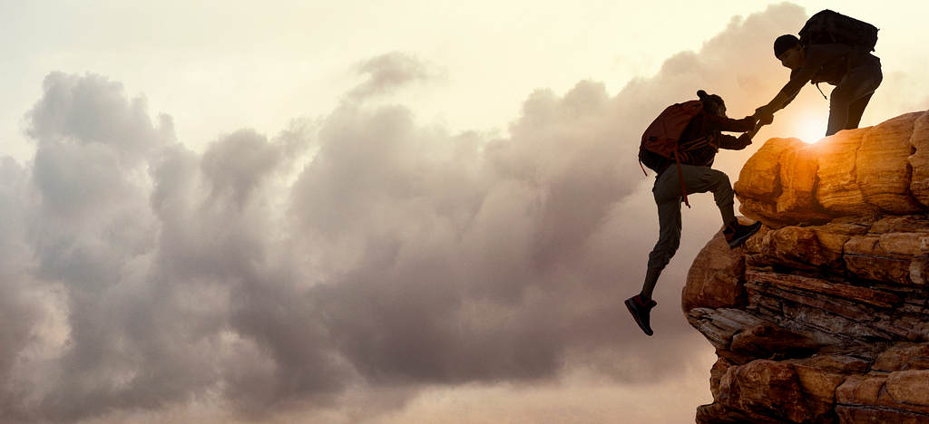 Two people climbing a cliff. One person is assisting the other up the cliff.