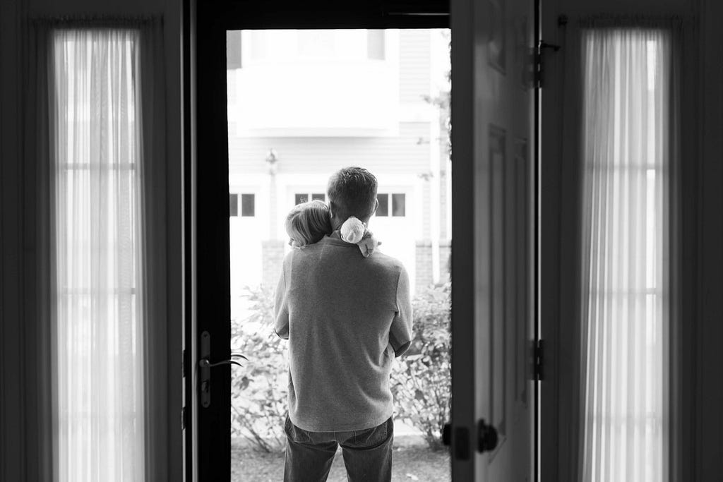 A black-and-white photo of a father holding his young daughter in a doorway