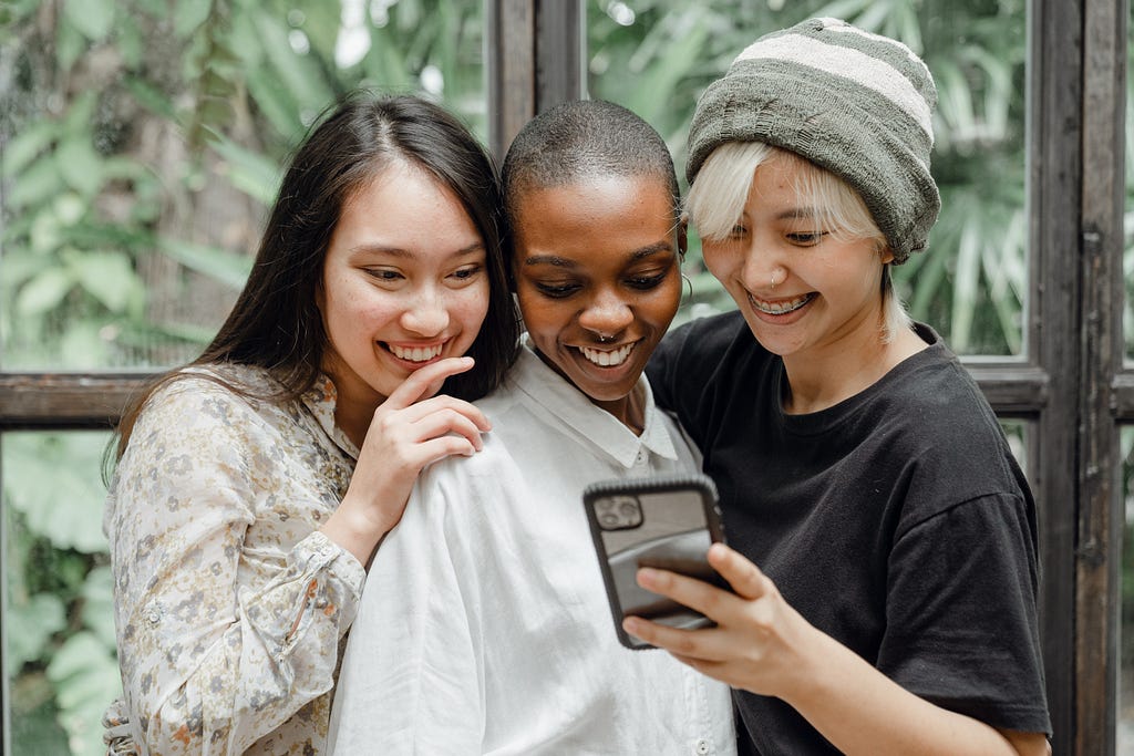 Three women standing together looking at a cellphone screen and smiling