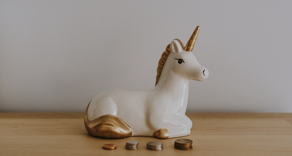 a statue of a white unicorn with a golden horn and tail, four piles of coins lying in front of it