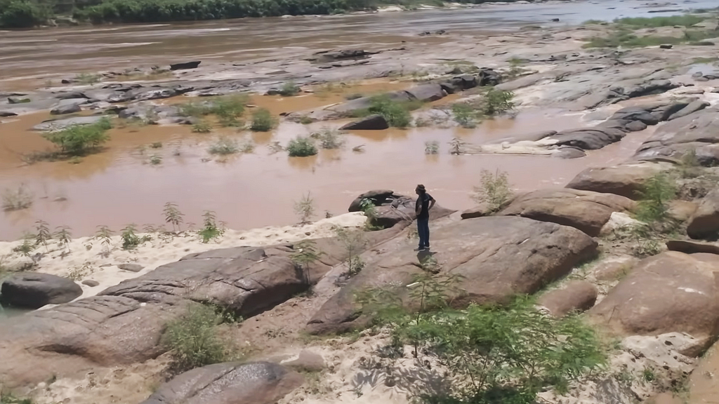 Foto de um homem, em pé, em meio às pedras de um rio.