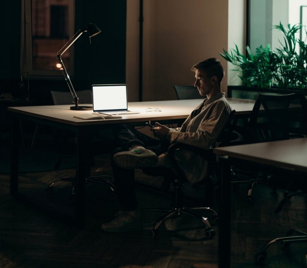 A man looking away from the computer and focusing on his phone