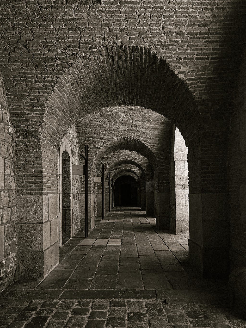 A black and white photo of the arches and corridors surrounding the parade ground, with its brick walls.