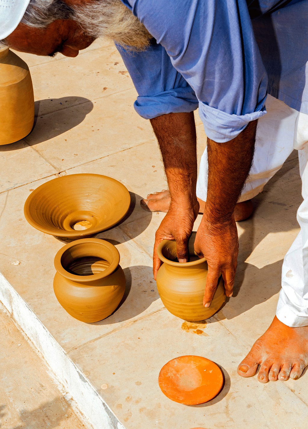 A man shapes a series of unfired clay vessels.