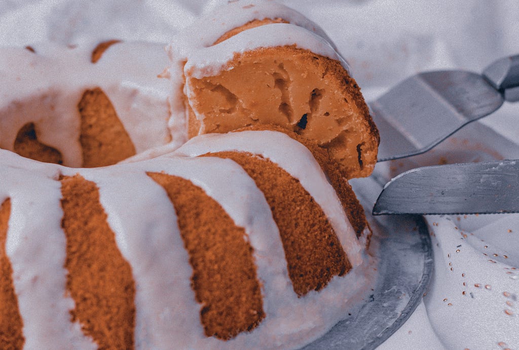 A imagem mostra um bolo de laranja sendo cortado e tendo uma fatia retirada