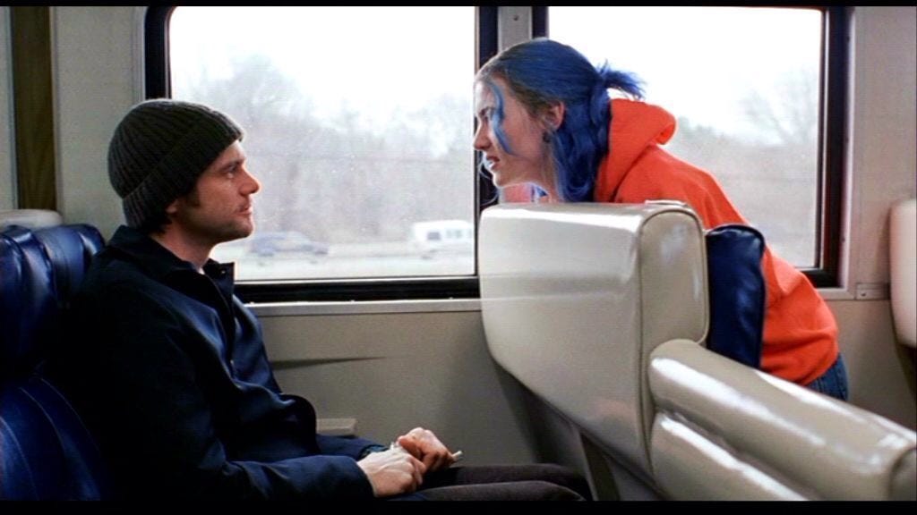 Clementine turns and sits up from her seat on a train to speak to Joel, who is seated behind her.