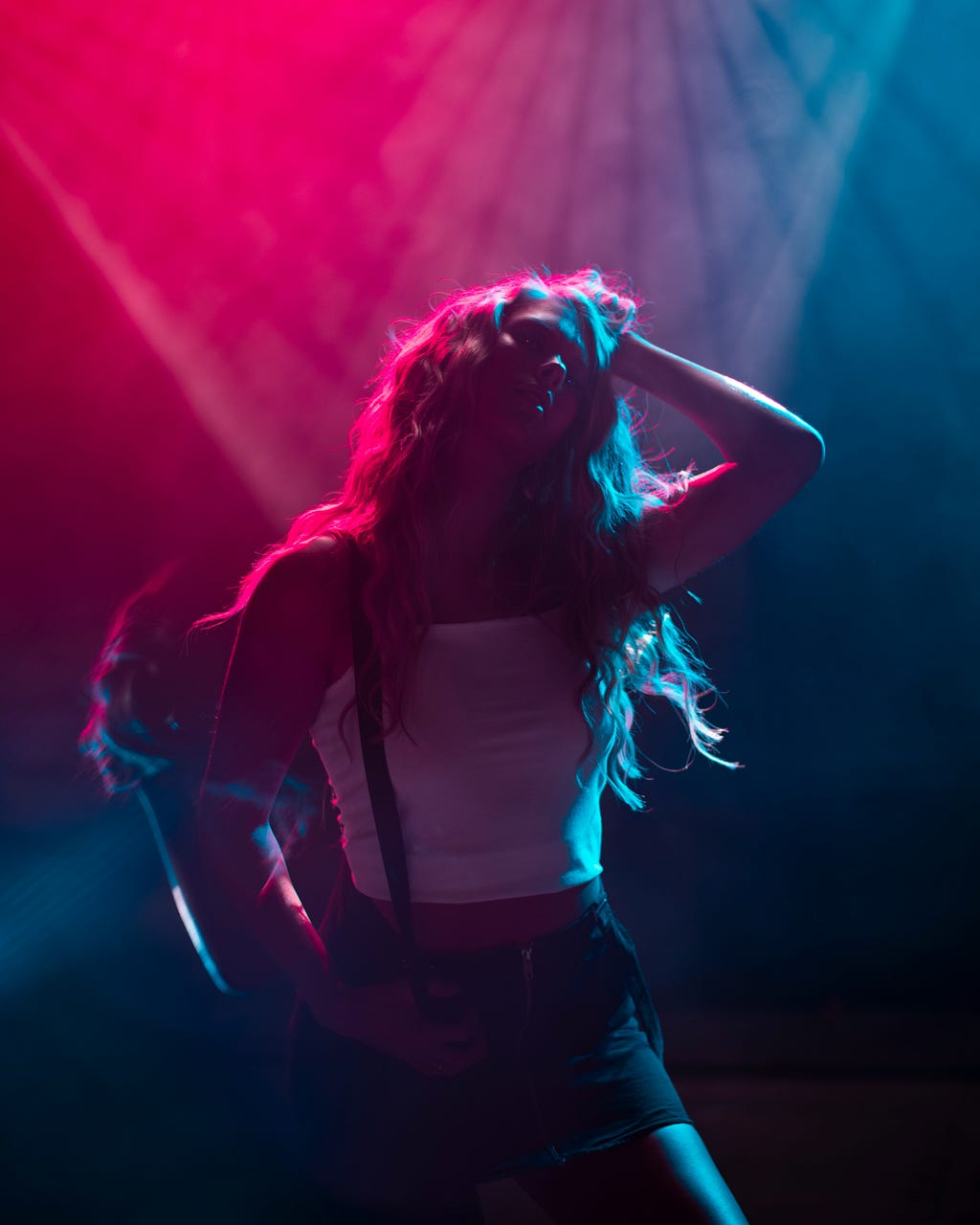 A woman wearing black pants and a white tank top dancing under the red and blue lights of a nightclub.