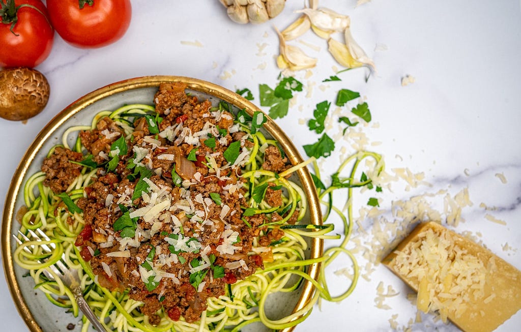 A bowl of zucchini noodles with an Italian ground beef and tomato sauce on top.