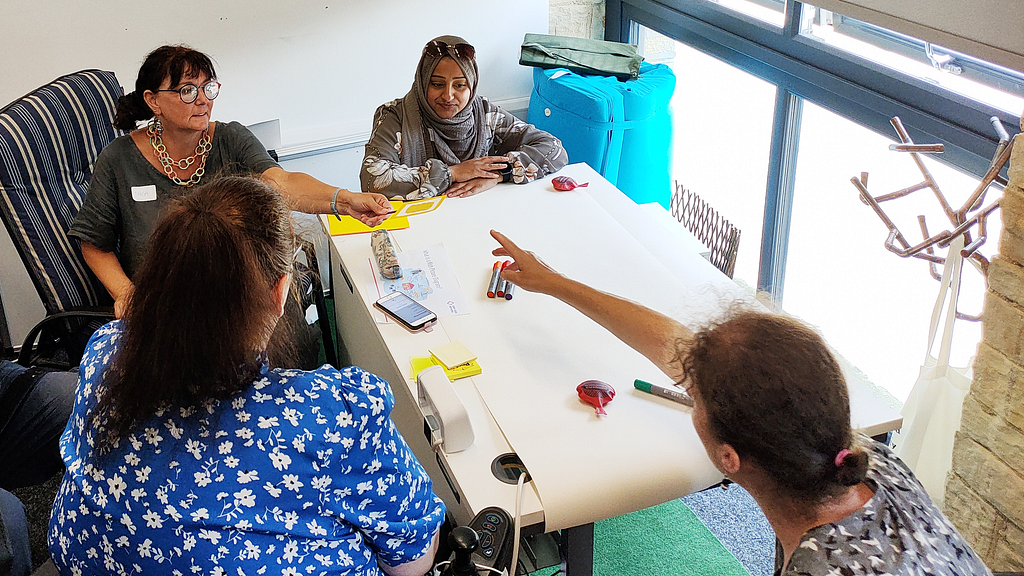 Four participants of the Strengthening Social Care workshop sit around a table with paper and pens.