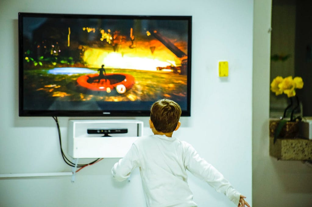 Foto de um menino se aproximando de um aparelho de televisão instalado numa parede.