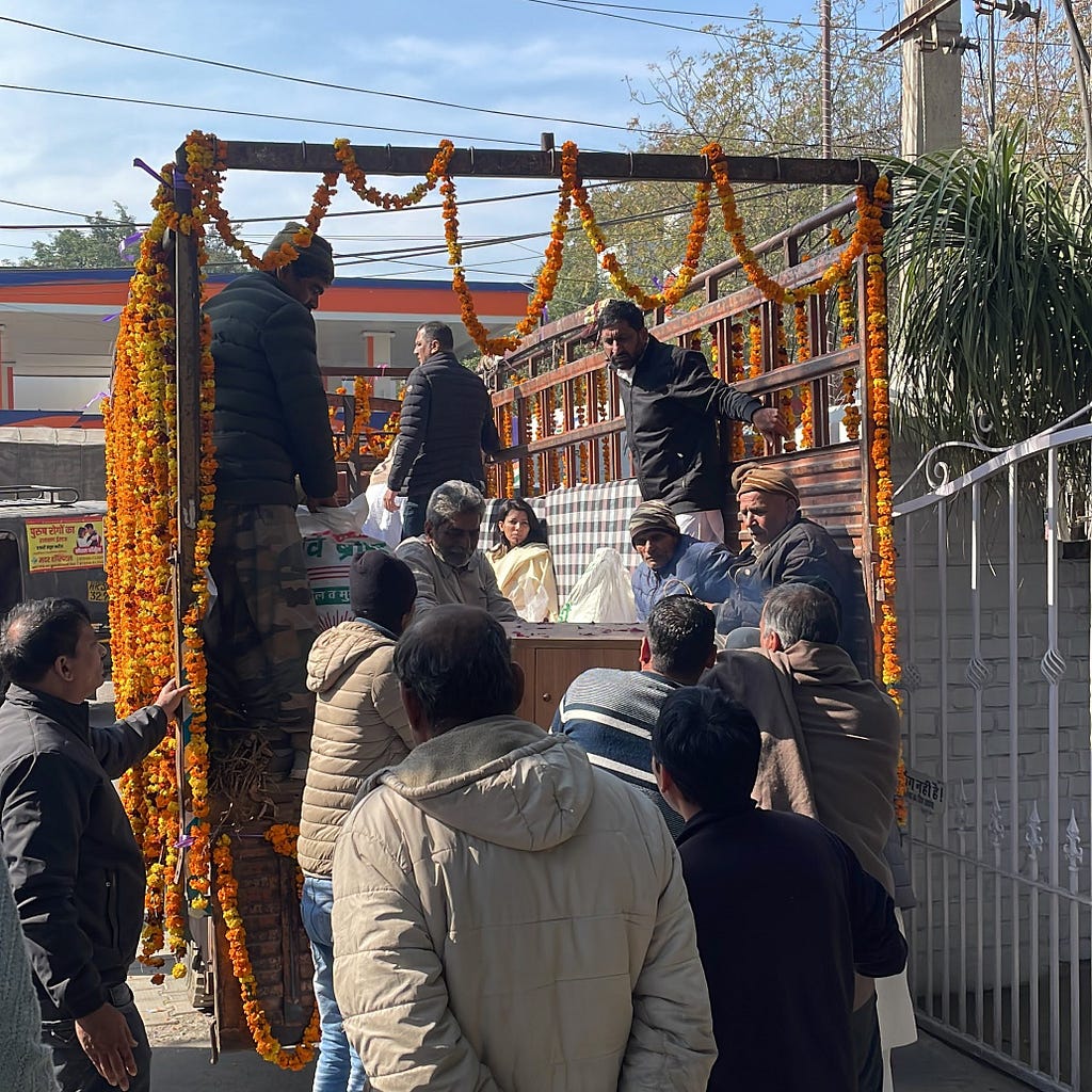 Truck decorated with marigolds. People are sitting and standing in the back of the truck while others are watching.