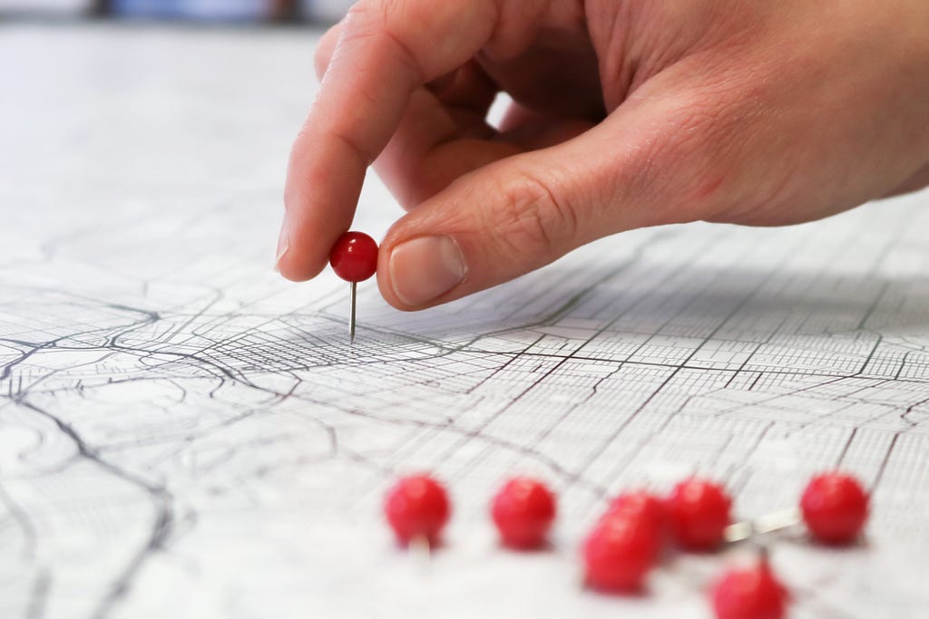 A close-up of a hand placing red pins on a map.
