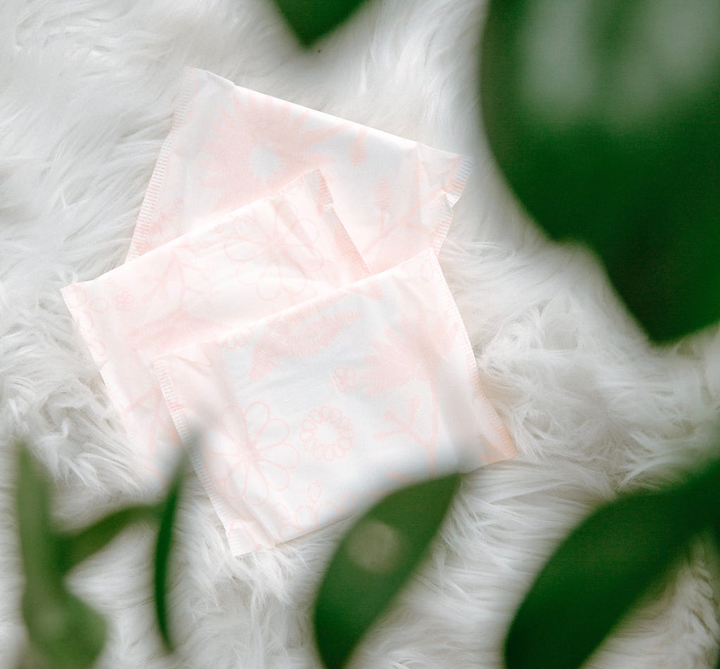 Sanitary pads nestled on white fur under an overhang of greenery