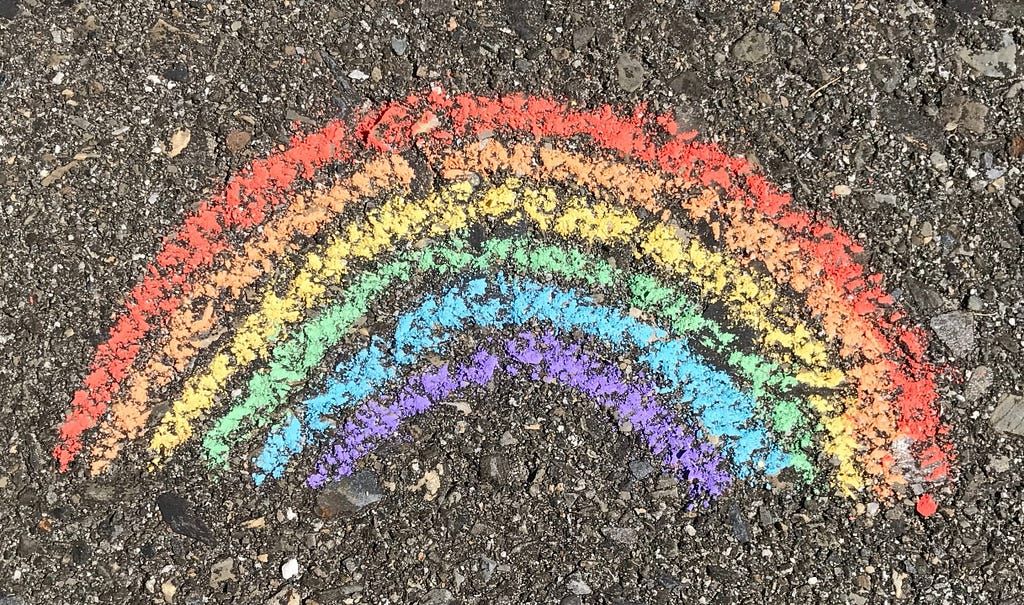 A rainbow with red, orange, yellow, green, blue, purple, drawn with chalk on concrete.