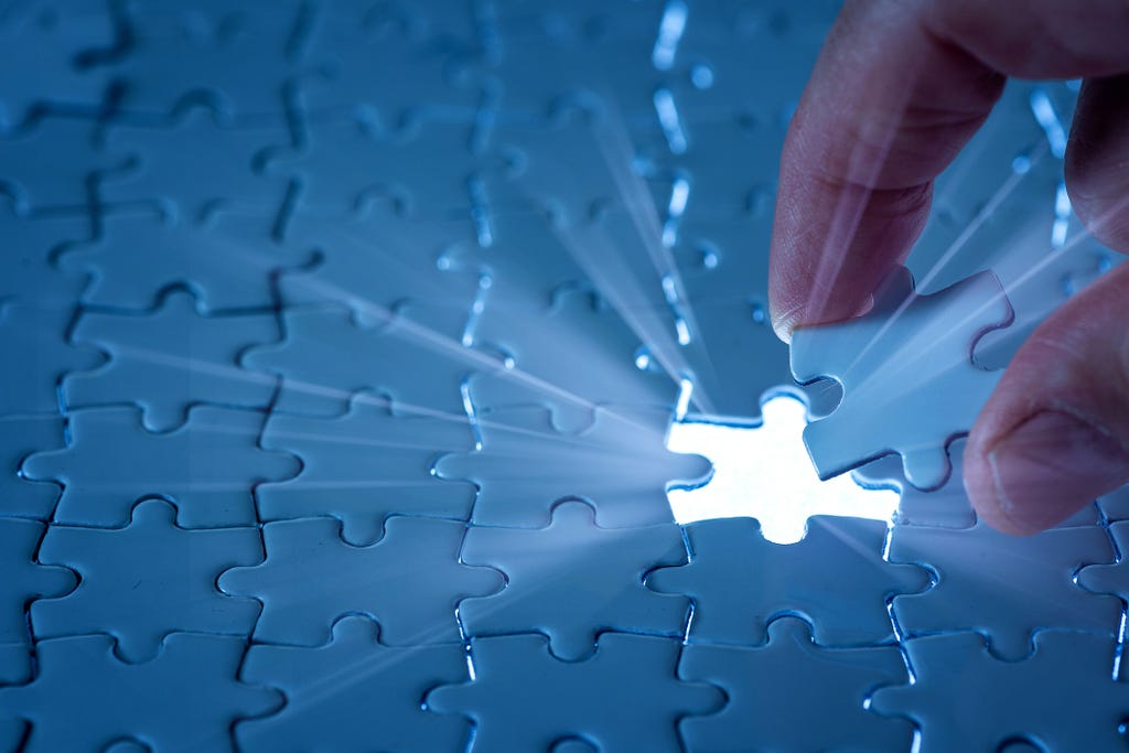 Close up of a hand placing the final piece of an entirely blue jigsaw puzzle.